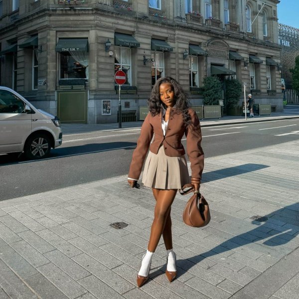 All brown outfit idea for fall. Womanw earing brown cropped blazer and pleasted skirt with heels nad socks. 