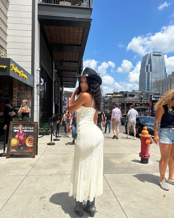 Cute nasville outfit idea. Black woman wearing white dress, black cowboy boots and cowboy hat.