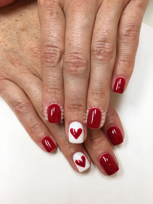 Pretty short red nails with a tinny red heart design on one white nail polish