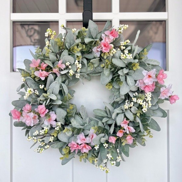 A spring wreath with pink and yellow flowers hanging on a wooden front door