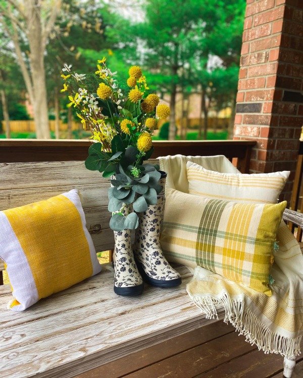 Yellow daffodils in a vase on a porch table with a yellow throw pillow nearby.