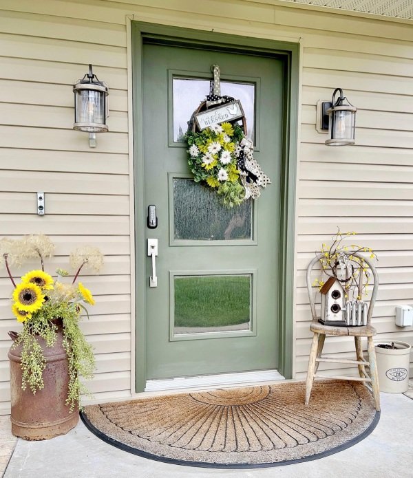 A rustic birdhouse hanging from a porch beam with blooming flowers below.