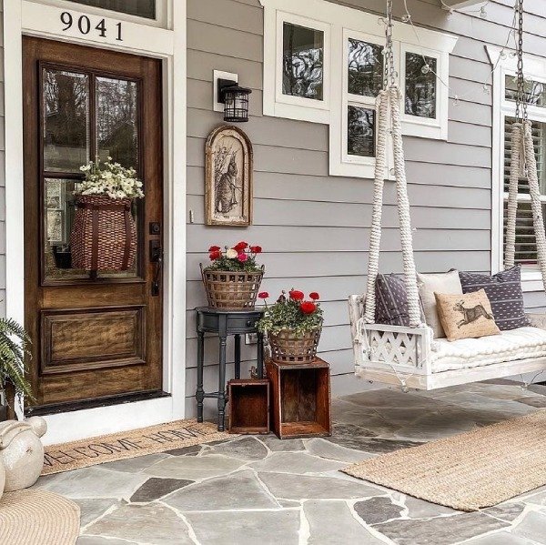 A white porch swing with pastel cushions and a blooming flower pot nearby.