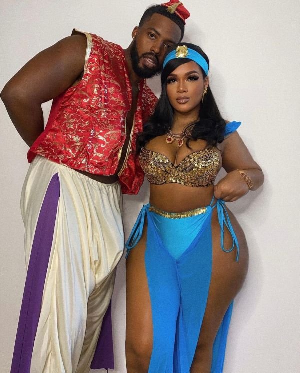A Black couple embodies Jasmine and Aladdin in turquoise and gold costumes, complete with a magic lamp prop. The look is colorful, romantic, and straight out of Agrabah.
