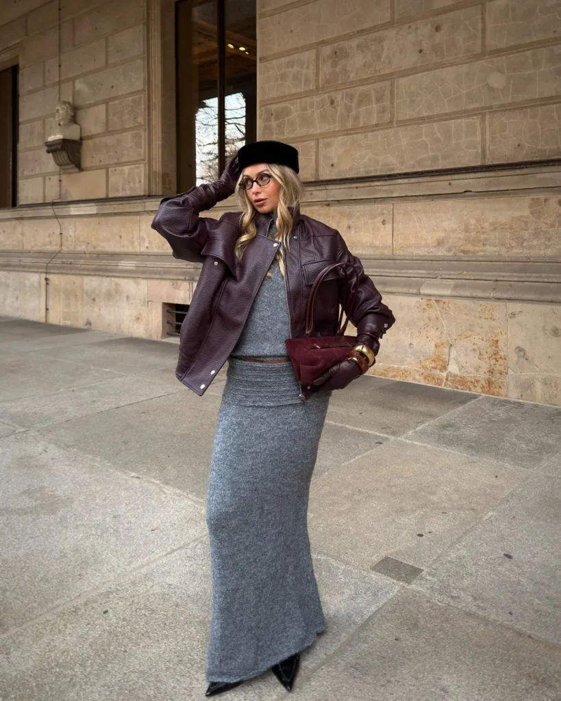This image shows a person wearing a grey dress, a burgundy leather jacket, matching gloves and handbag, and a black hat.
