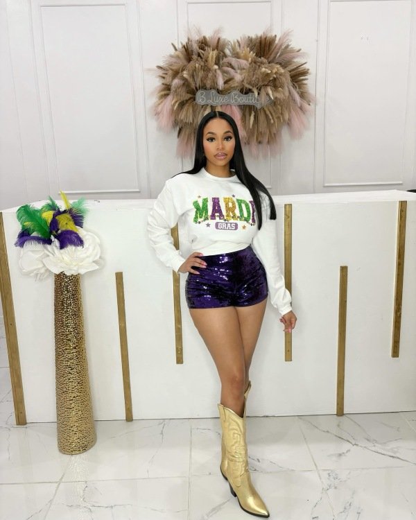 White graphic long sleeve top styled with sparkling sequin pants for a festive Mardi Gras look.