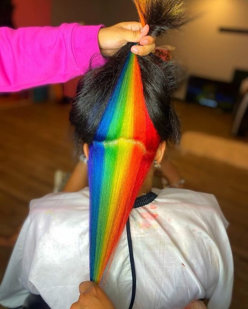 Long dark hair with hidden rainbow peekaboo highlights underneath, showing multiple vibrant colors.