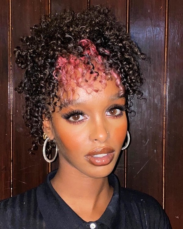 Rose Pink Curls peekaboo highlight. Woman with natural curly hair black and pink dye hair in the front.