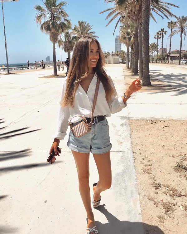 Casual Hawaii vacation outfit with denim shorts, oversized button-up shirt, and beach sandals.