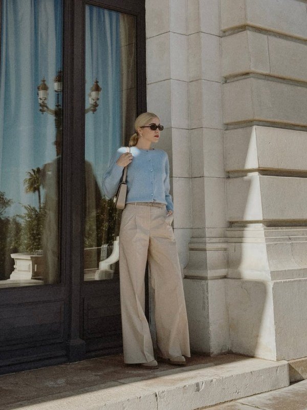 Woman wearing taupe wide-leg pants with a blue cropped sweater, brown ankle boots, and a small handbag for a cozy fall outfit.