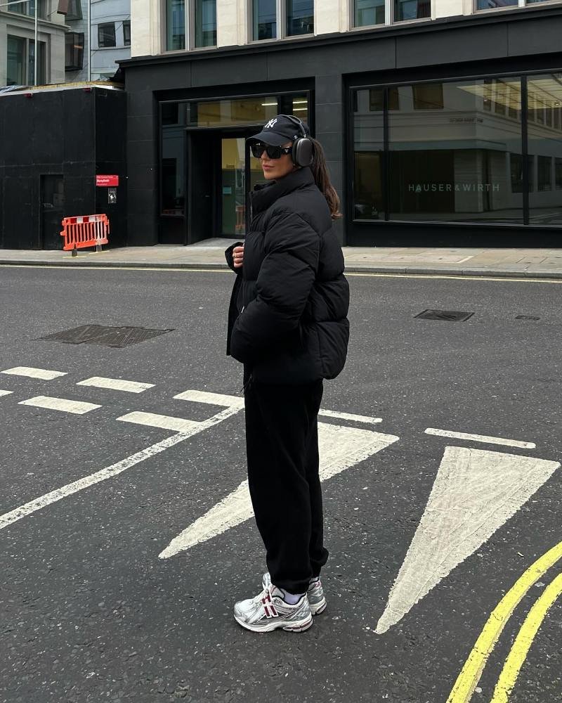 Woman wearing a cozy puffer jacket with black sweatpants and casual sneakers for a warm cold-weather outfit.