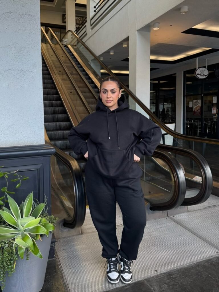 Woman wearing a relaxed hoodie with black sweatpants and sneakers for a comfortable sporty everyday outfit.