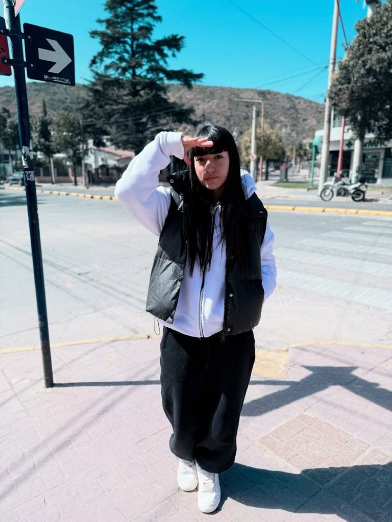 Woman wearing a black puffer vest with a wehite long sleeve sweatshirt black sweatpants, and casual sneakers for a cozy everyday outfit.