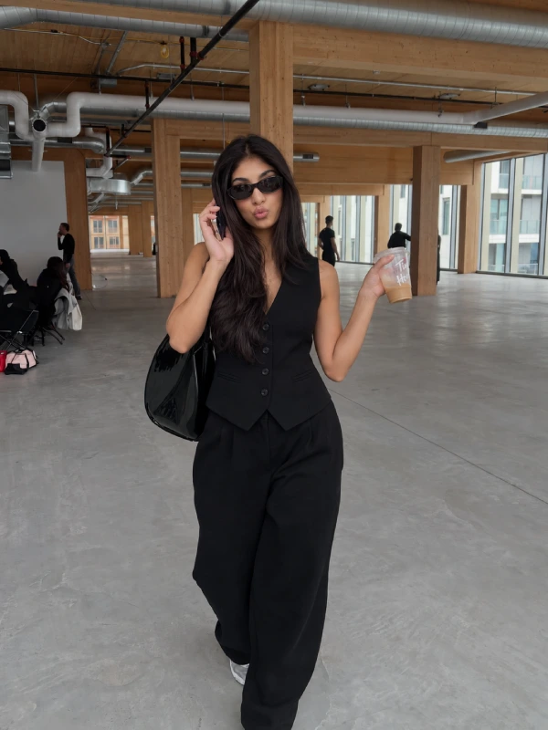 Woman styling a tailored vest with black sweatpants, a fitted top, and polished casual shoes for a modern elevated outfit.