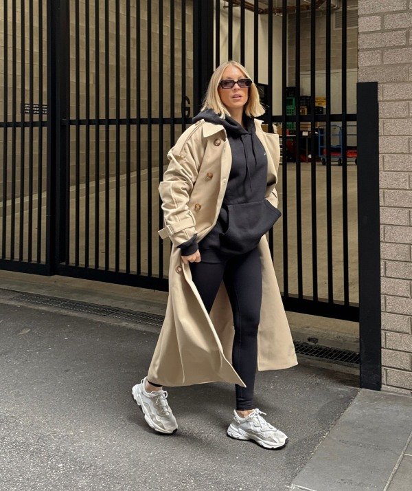 Relaxed street style outfit with a trench coat layered over a gray hoodie, casual pants and sneakers.