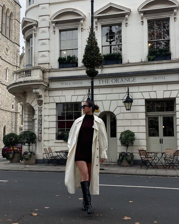 Stylish woman wearing a long trench coat with a mini skirt, fitted sweater and knee-high boots.