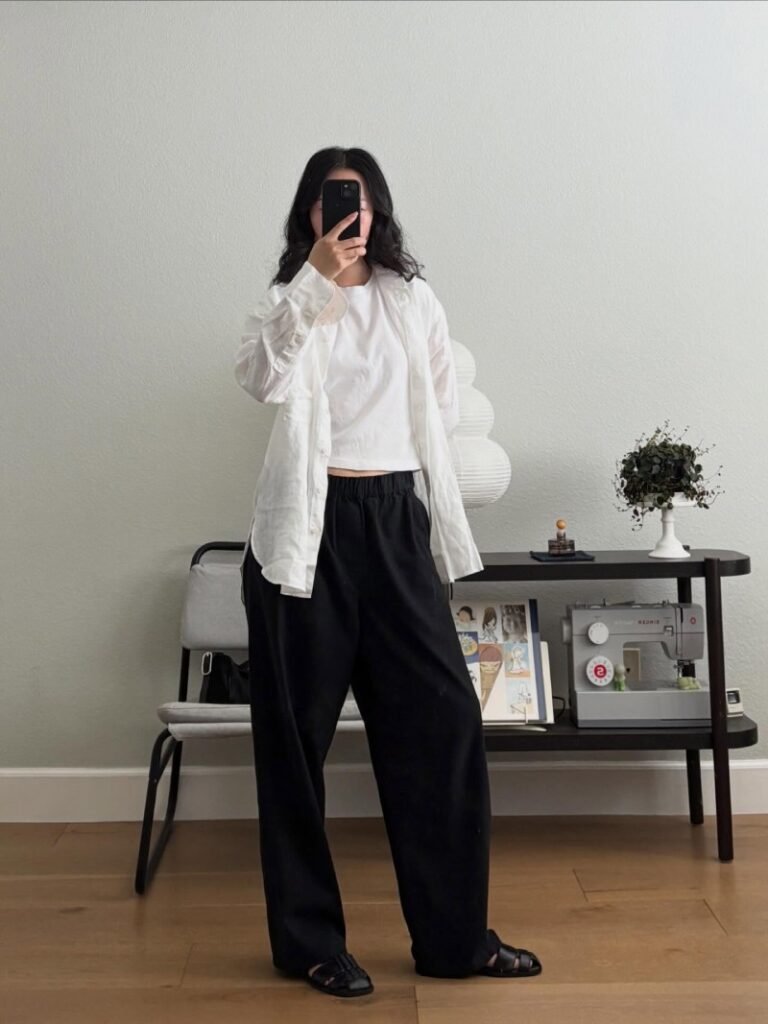Woman styling black sweatpants with an oversized button-down shirt, fitted tank top, and casual shoes for a relaxed polished outfit.