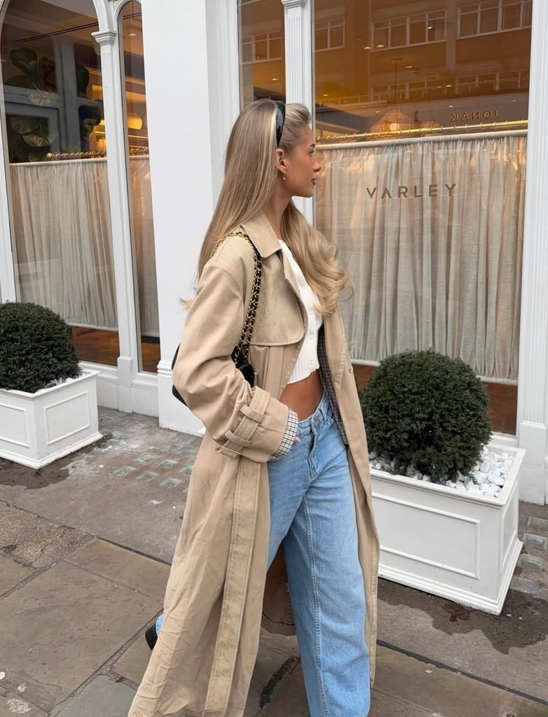 Woman wearing a classic beige trench coat with straight-leg blue jeans, white T-shirt and casual flats.