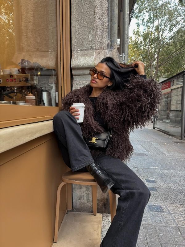 Woman pairing a faux-fur coat and black outfit with tall black cowboy boots on a winter street.